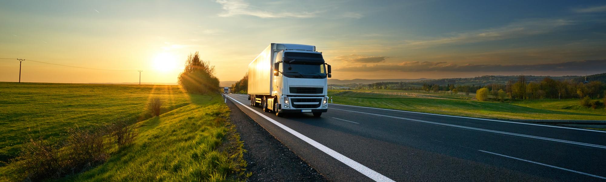 White truck driving on the asphalt road in rural landscape at sunset